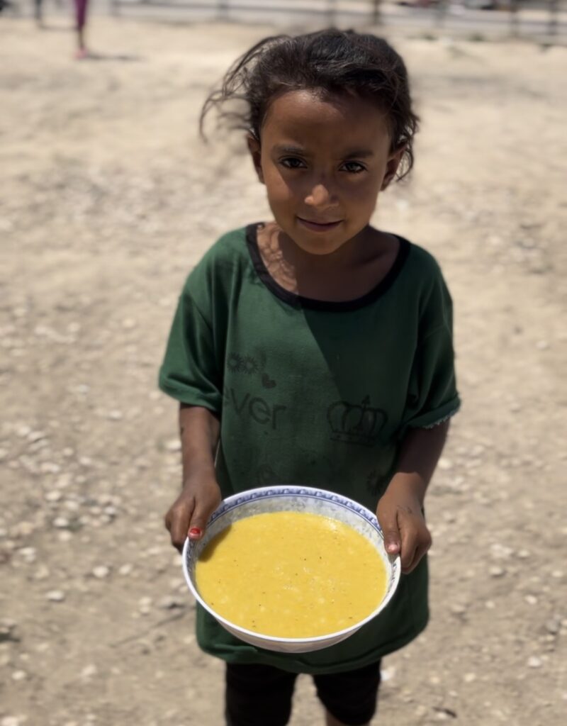 Jong meisje dat buiten een kom warme gele soep vasthoudt in een noodsituatie.