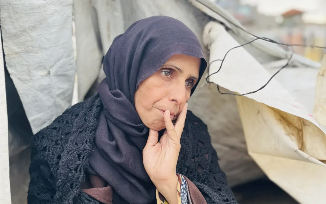 Vrouw in donkere kleding zit voor een geïmproviseerde tent in Gaza, kijkt bezorgd in de verte