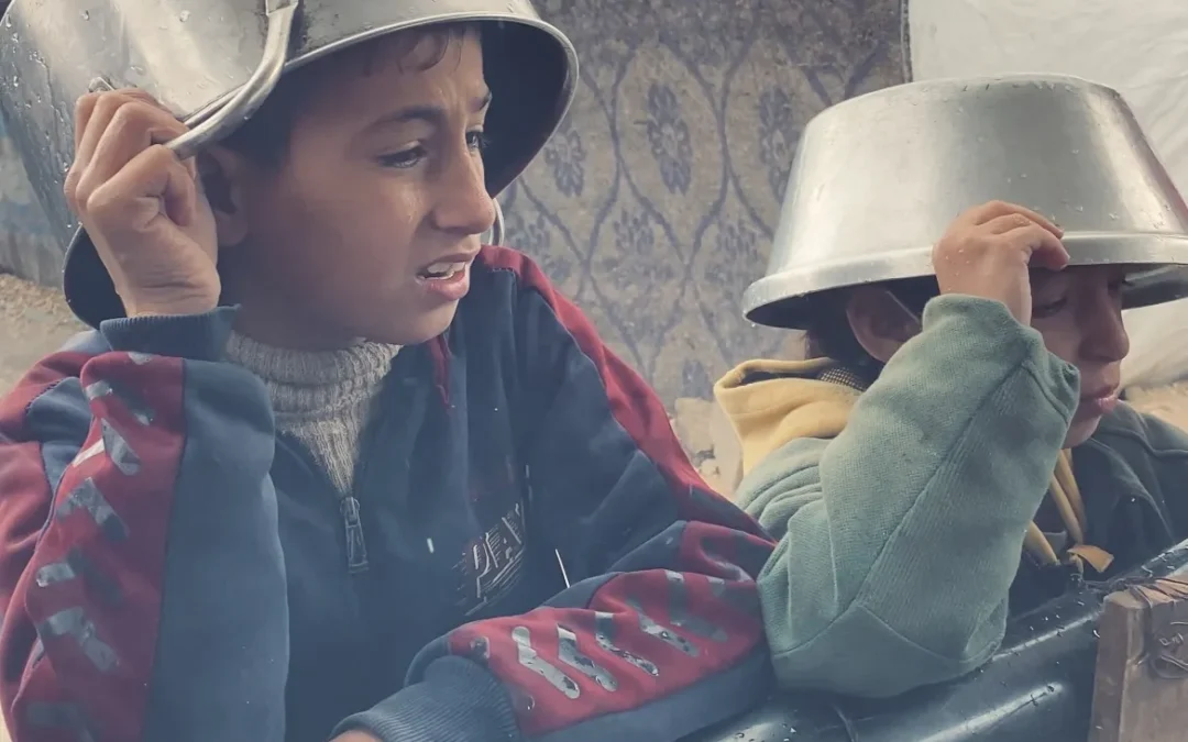 Twee jongens in vluchtelingenkamp in Gaza dragen metalen potten op hun hoofd als bescherming tegen regen
