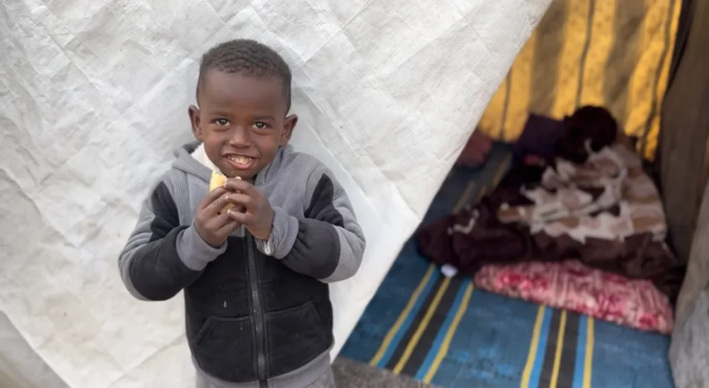 Jonge jongen eet glimlachend een stuk fruit voor een tent