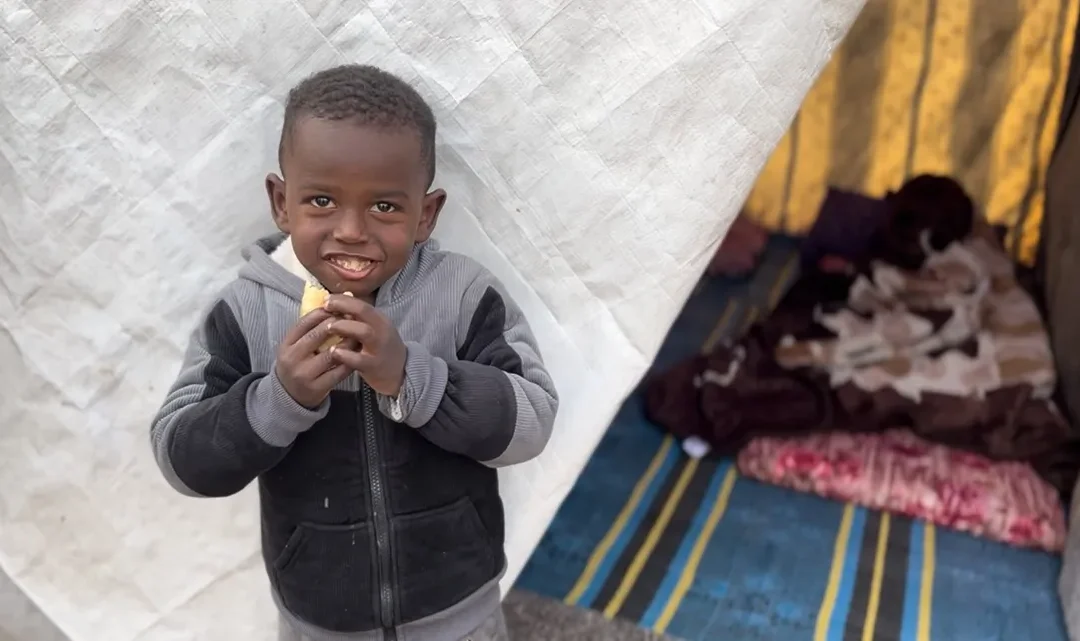Jonge jongen eet glimlachend een stuk fruit voor een tent