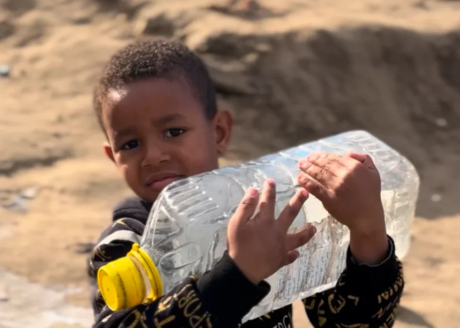 Kind draagt zware plastic waterfles op droge, zanderige ondergrond