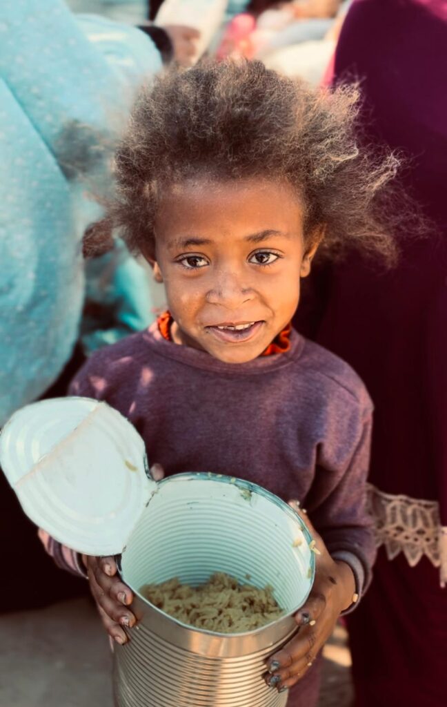Kind met een blik eten in de hand tijdens een voedseluitdeling in een noodsituatie.