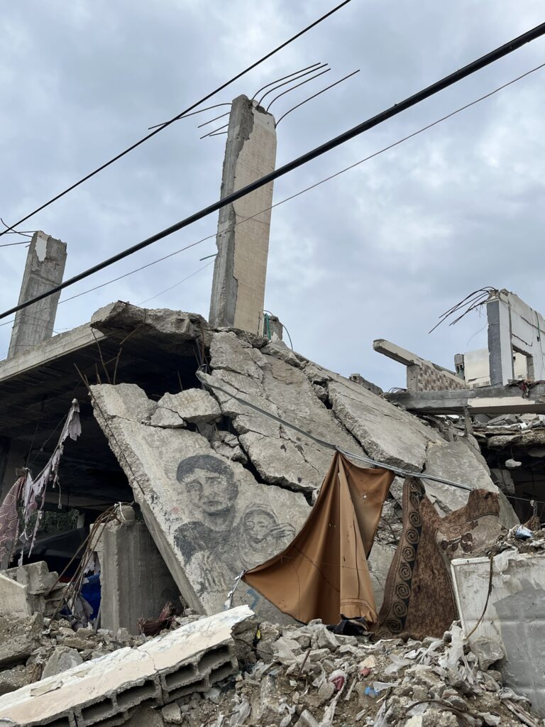 Verwoest betonnen gebouw met zichtbaar muurportret van man en kind tussen het puin, onder een bewolkte hemel