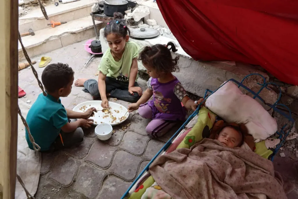 Kinderen in een noodsituatie eten samen naast een slapende baby, in een geïmproviseerde schuilplaats.