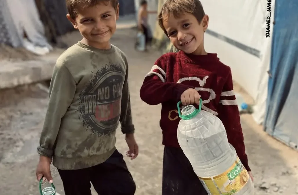 Twee kinderen dragen grote waterflessen in een kamp, symbool voor toegang tot schoon drinkwater